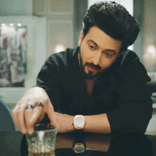 a man wearing a watch is sitting at a table with a glass of whiskey