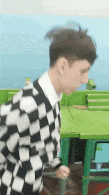 a young man in a black and white checkered sweater is standing in front of a green table .