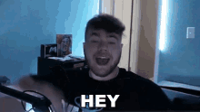 a man in a black shirt is saying " hey " in front of a microphone
