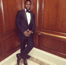 a man in a tuxedo and bow tie stands with his hands folded