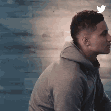 a man in a gray hoodie is sitting in front of a wooden wall and has a bird on his head .