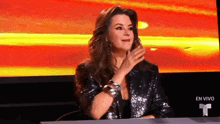 a woman in a sequined jacket is sitting at a table in front of an en vivo sign
