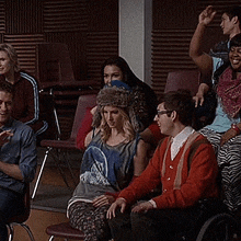 a group of people are sitting in chairs in a room with a man in a wheelchair