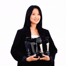 a woman in a black jacket is holding a stack of trophies