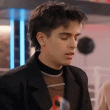 a young man wearing a black jacket and a black turtleneck is standing in a room .