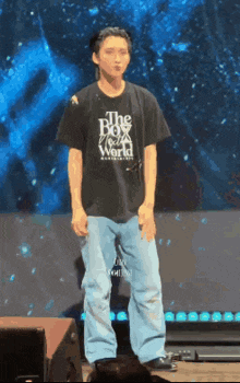 a man wearing a black t-shirt that says the boy next world is standing on a stage .