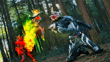 a man in a black and white suit is kneeling down in the woods with a fireball coming out of his hand
