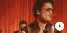 a man wearing sunglasses and a suit is standing in front of a red curtain .