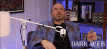 a man is sitting in front of a microphone with the words dark web written on the bottom of the screen .
