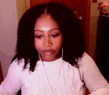 a woman with curly hair is wearing headphones and a white sweater while sitting in a chair .