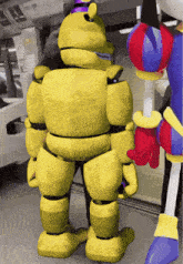 a yellow robot with a purple hat is standing next to another robot