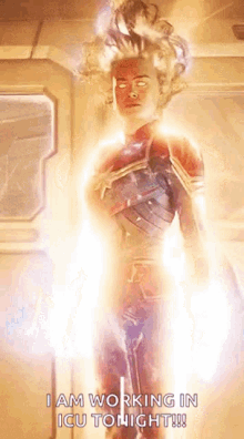 captain marvel is standing in a room with a light coming out of her chest .