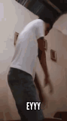 a man in a white shirt is dancing in a room with the word eyyy written on the bottom of his shirt .