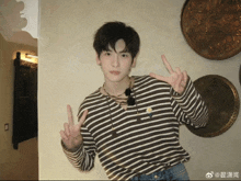 a young man wearing a striped shirt is giving a peace sign