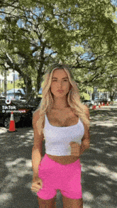 a woman in a white tank top and pink shorts is standing in front of trees