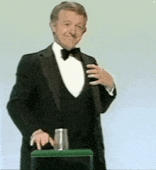 a man in a tuxedo and bow tie is standing next to a green stool .