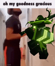 a man standing next to a green robot that says oh my goodness gracious on it