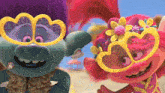 two trolls wearing heart shaped sunglasses are standing on a beach .