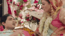 a bride and groom are sitting next to each other in a room decorated with flowers and garlands .