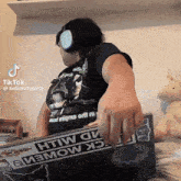 a woman wearing headphones and a shirt that says hellokittytorta holds a laptop