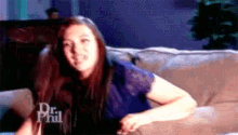 a woman is sitting on a couch wearing a blue shirt that says dr phil