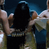 a woman with long black hair is surrounded by two other women in gold