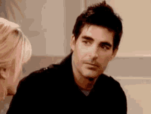 a man in a black jacket is talking to a woman