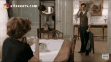 a man talking on a cell phone in a room with eltrecetv.com