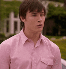 a young man wearing a pink shirt is looking at something