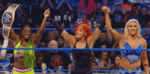 a group of female wrestlers are standing in a ring holding their fists in the air .