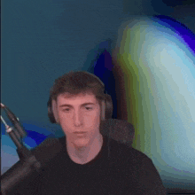 a young man wearing headphones and a black shirt is standing in front of a microphone .