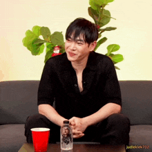 a man is sitting on a couch with a red cup and a bottle of water in front of him