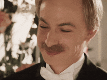 a man with a mustache wearing a tuxedo and bow tie smiles