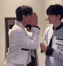 two men are standing next to each other in front of a mirror and one of them is whispering into the other 's ear