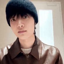 a man wearing a black hat and a brown jacket looks at the camera