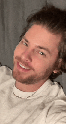 a man with a beard wearing a white shirt and a silver chain around his neck