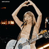 a woman is singing into a microphone while holding a guitar and making a heart shape with her hands