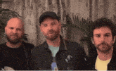 three men standing next to each other with one wearing a baseball cap