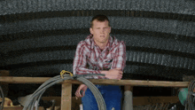 a man in a plaid shirt is sitting on a wooden railing