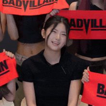 a girl in a black shirt is smiling while holding a red badvillain towel