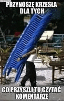 a man is carrying a pile of blue chairs on his back .