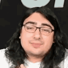 a man with long hair and glasses is smiling in front of a black background .