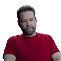 a man with a beard is wearing a red shirt and making a sad face