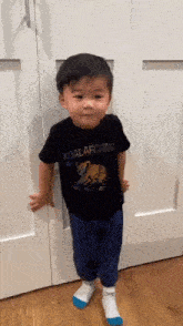 a little boy is standing in front of a door wearing a koalaforma t-shirt .