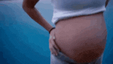 a close up of a woman 's belly in a white shirt against a blue background .
