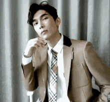 a man in a suit and tie is sitting in front of a curtain and looking at the camera .