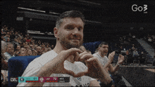 a man making a heart shape with his hands while watching a basketball game