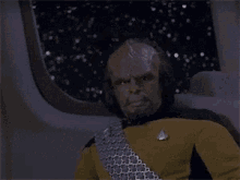 a man with a beard is sitting in a chair in front of a window on a space ship .