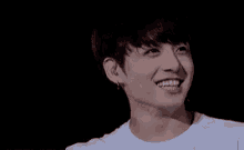 a close up of a young man wearing a white shirt and earrings smiling .
