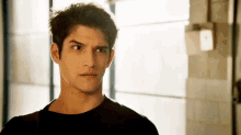 a young man in a black shirt is standing in front of a window and looking at the camera .
